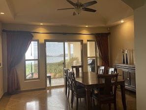 A dining area with a table and chairs, a ceiling fan, and a view of a balcony with a grill.