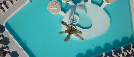 An aerial view of a swimming pool with multiple sun loungers and a central palm tree.