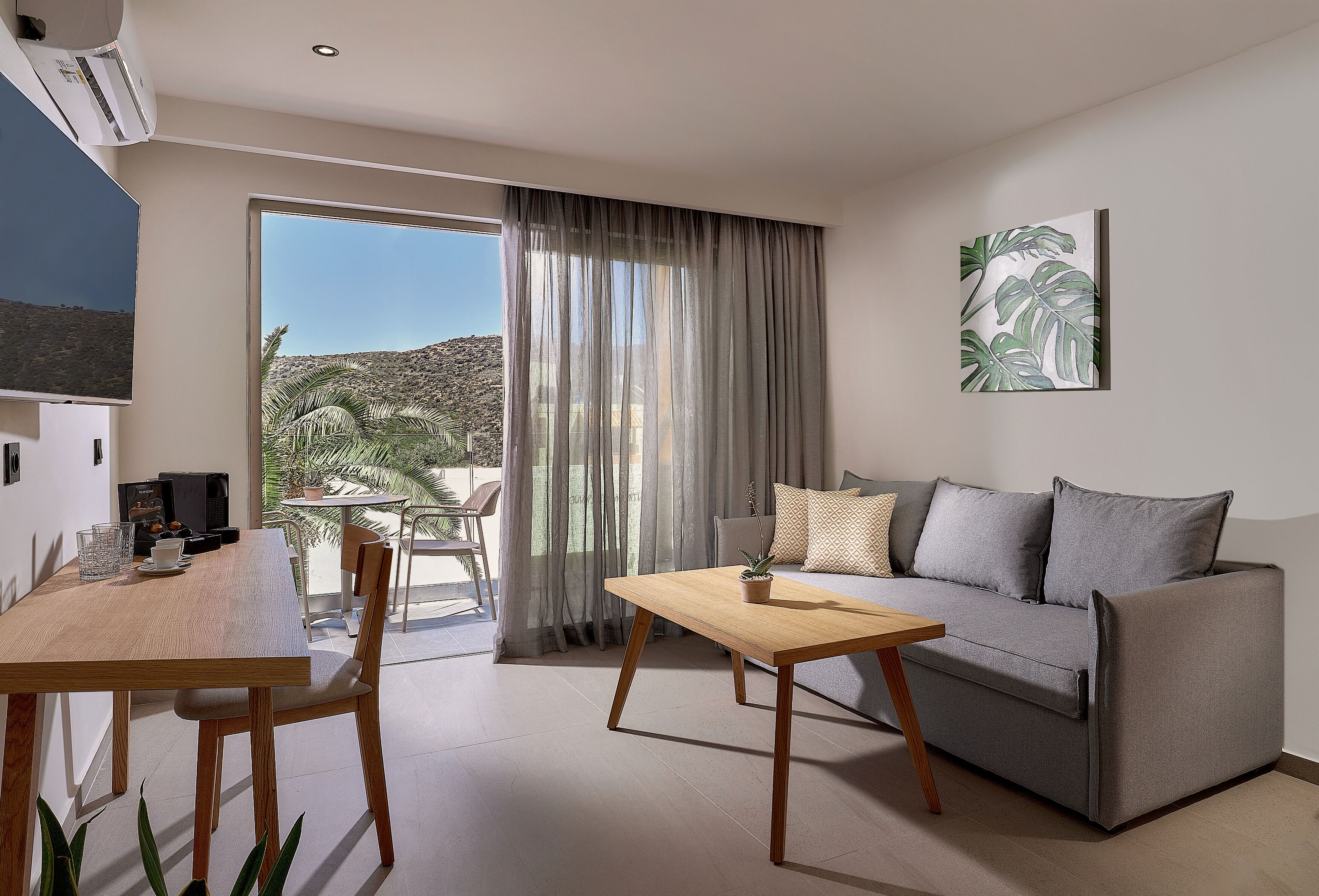 A modern living room with a grey sofa, wooden coffee table, and a dining table with chairs.