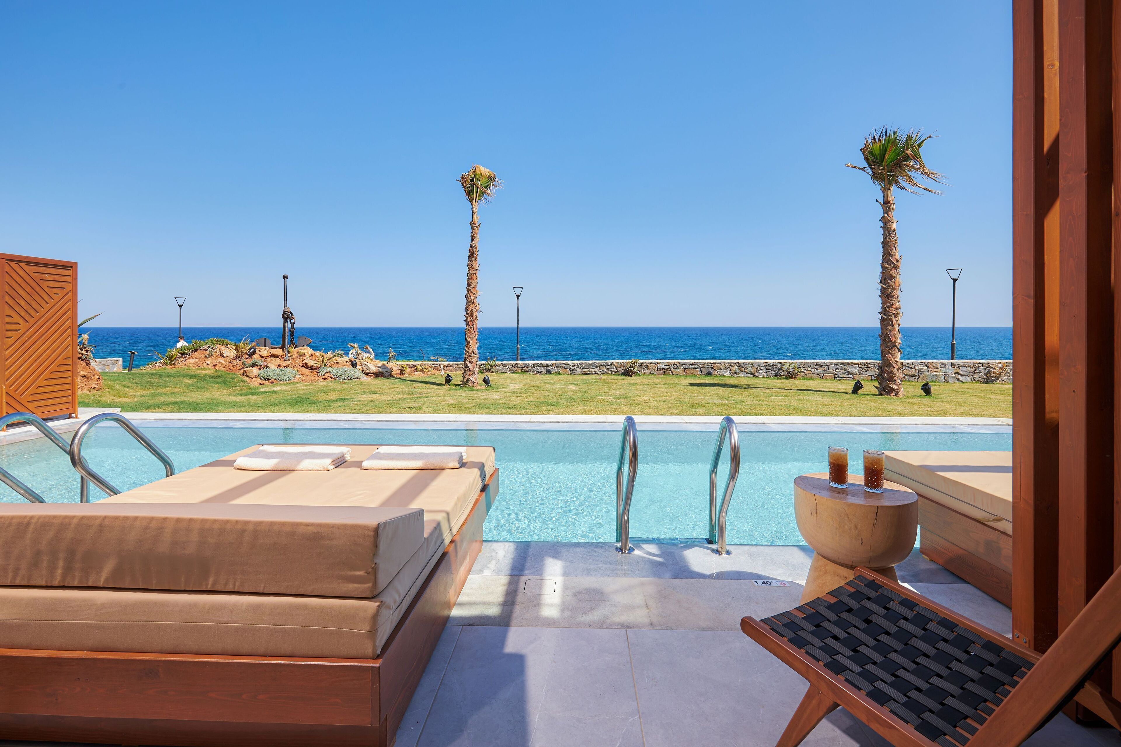 A poolside area with lounge chairs, a wooden deck, and a view of the ocean.