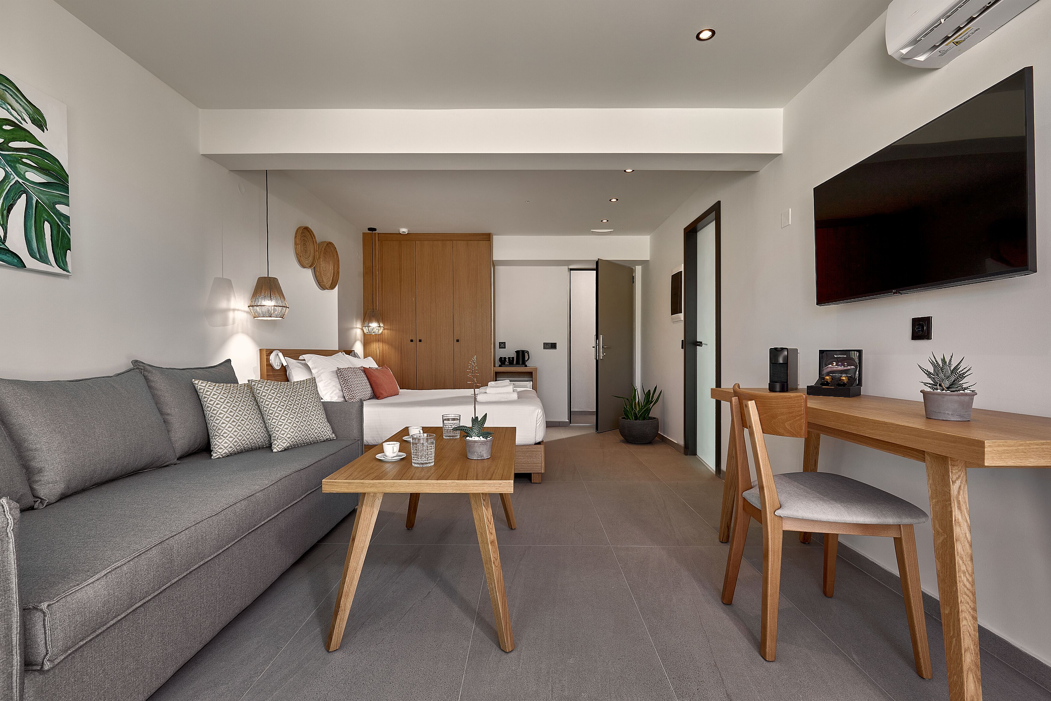 Ein modernes Wohnzimmer mit grauem Sofa, Couchtisch aus Holz und einem Essbereich mit Holztisch und Stuhl.