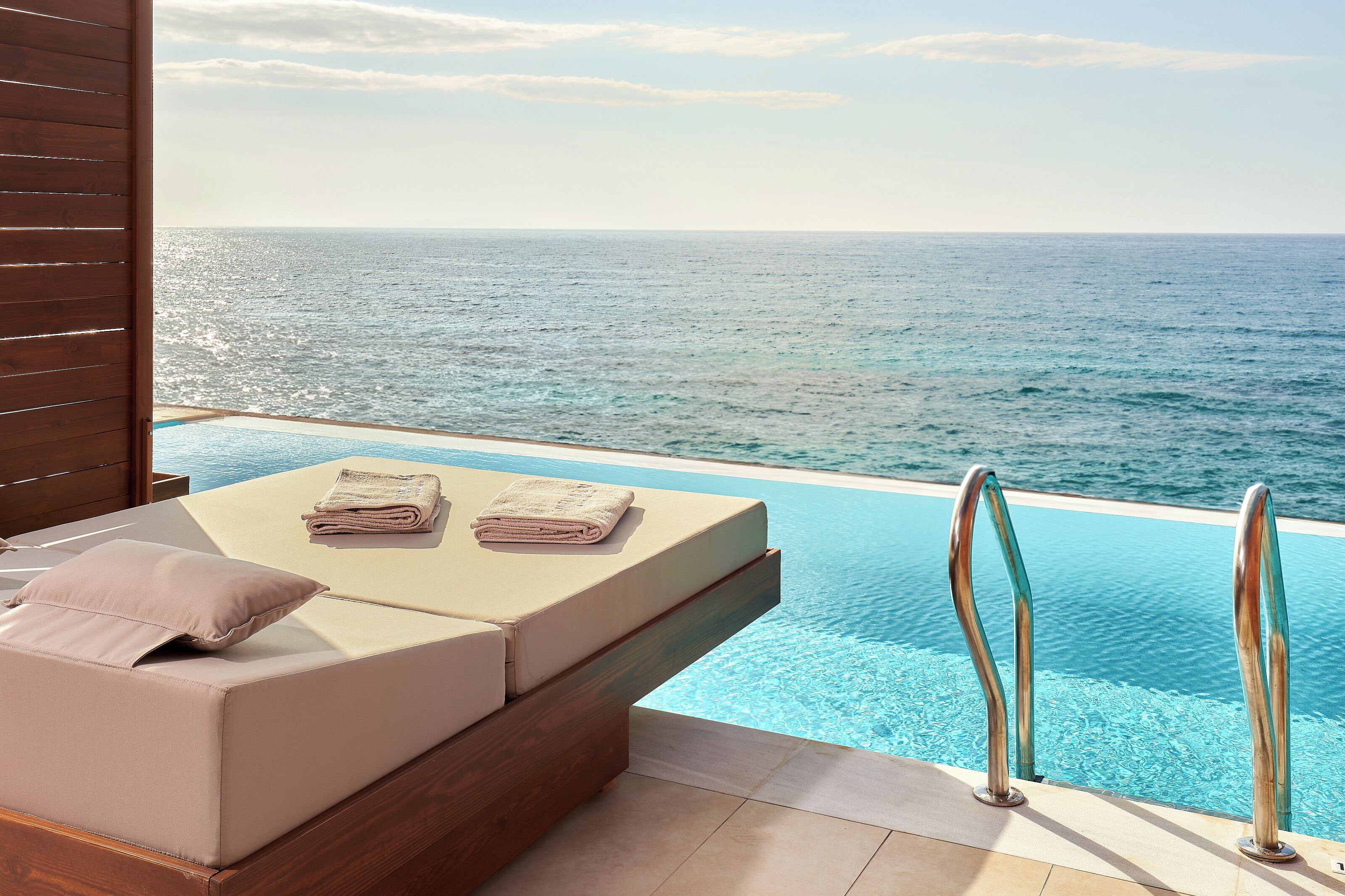 Un área de descanso junto a la piscina con vista al océano, una terraza de madera y una pequeña mesa con toallas.