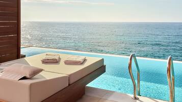 Un área de descanso junto a la piscina con vista al océano, una terraza de madera y una pequeña mesa con toallas.