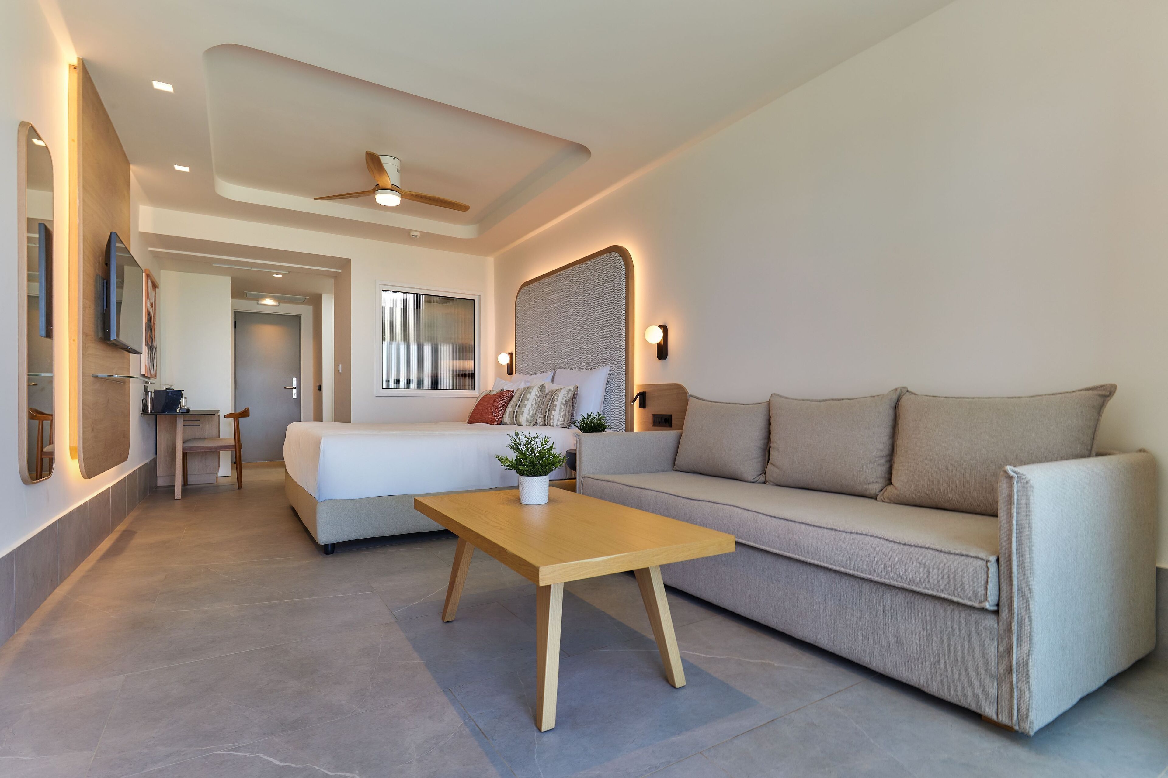 A modern living room with a sofa, a wooden coffee table, a TV mounted on the wall, and a ceiling fan.