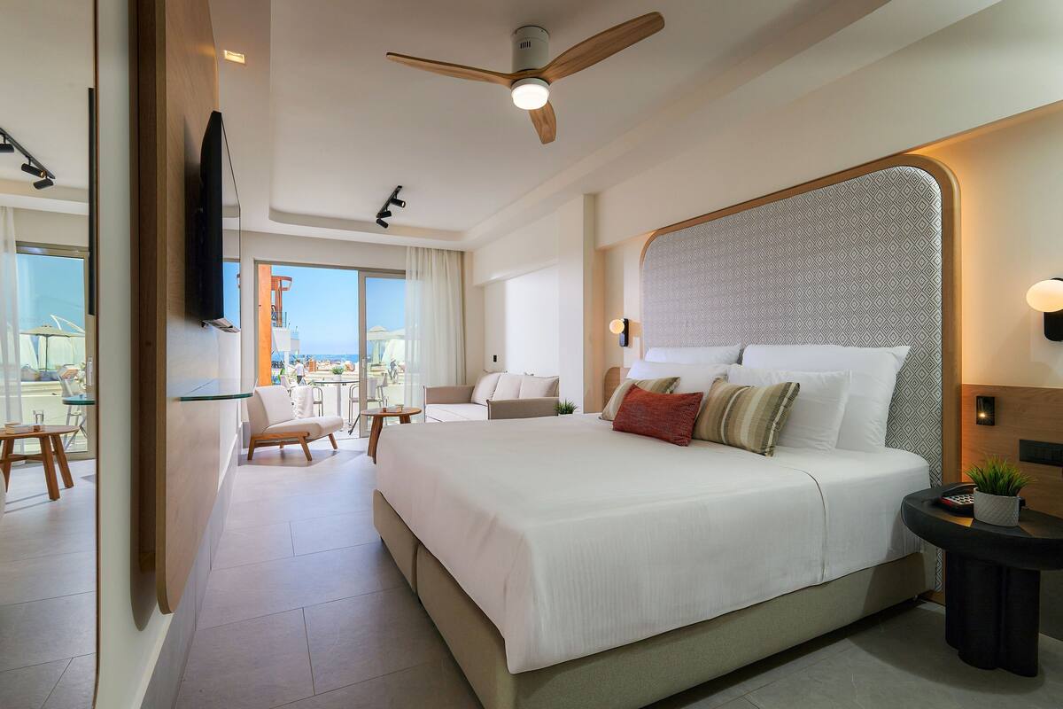 Een moderne hotelkamer met een groot bed, een plafondventilator, een aan de muur bevestigde televisie en een balkon met uitzicht.