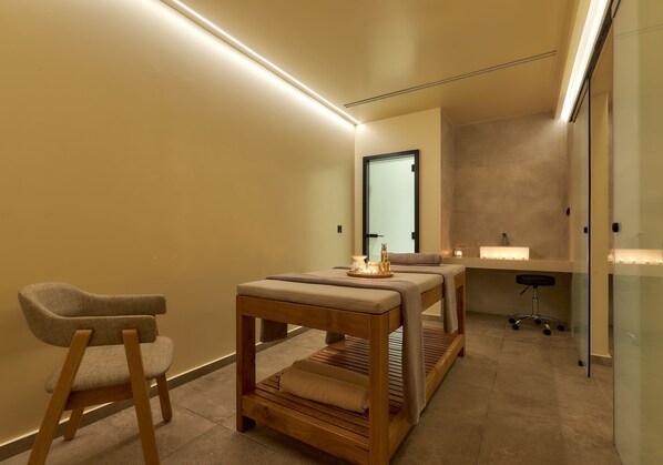Un cuarto de spa con una mesa de masaje, un banco de madera y una silla.