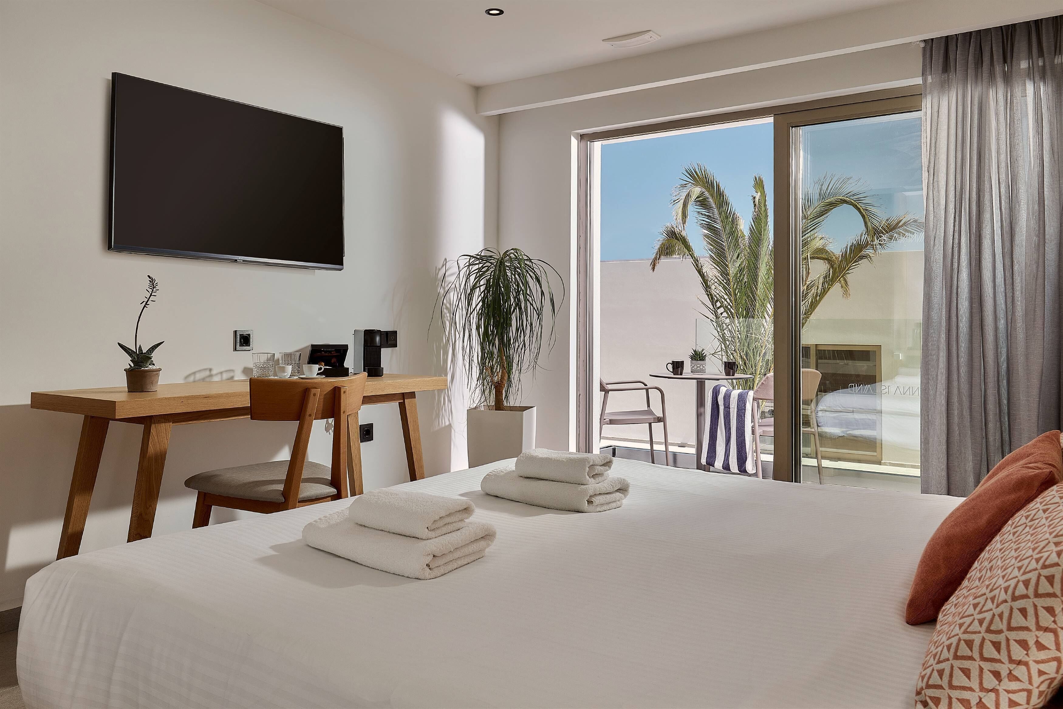 Une chambre d’hôtel équipée d’un lit, d’un bureau, d’une chaise, d’une télévision et d’un balcon agrémenté de plantes.
