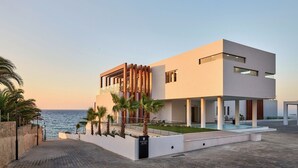 Un edifici modern de dues plantes amb piscina, a prop del mar.