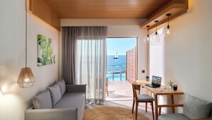 Un saló modern amb un sofà, una taula de menjador amb un ordinador portàtil, i vista al mar a través d'una finestra gran.