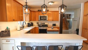 A kitchen with wooden cabinets, a large island with bar stools, stainless steel appliances, and hanging pendant lights. - Family Friendly Retreat, sleeps 12+, full basketball court, Large inground pool (La Porte)