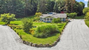 A house with a gravel driveway, surrounded by a well-maintained lawn and trees. - Family Friendly Retreat, sleeps 12+, full basketball court, Large inground pool (La Porte)