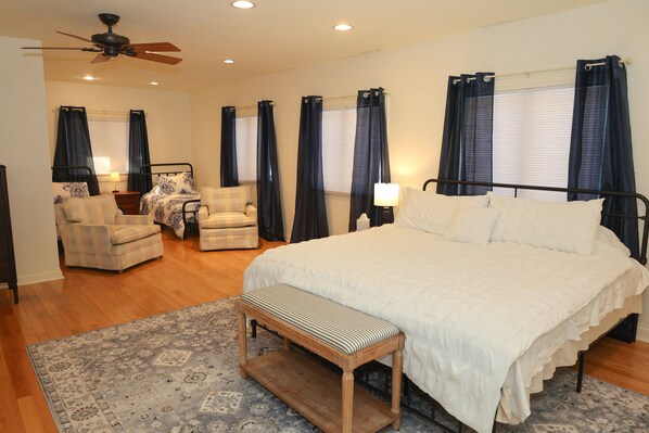 A bedroom with a large bed, two chairs, a bench, a ceiling fan, and a window with curtains. - Family Friendly Retreat, sleeps 12+, full basketball court, Large inground pool (La Porte)