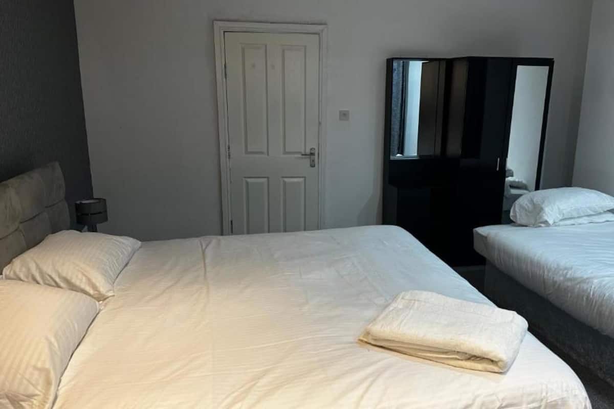 Ein Hotelzimmer mit zwei Betten, einer weißen Tür, einem Spiegel und einem Nachttisch mit einer Lampe.