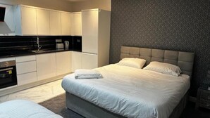 Une chambre d’hôtel moderne dotée d’un grand lit, d’un coin salon séparé, d’une kitchenette et d’un mur orné d’un motif.