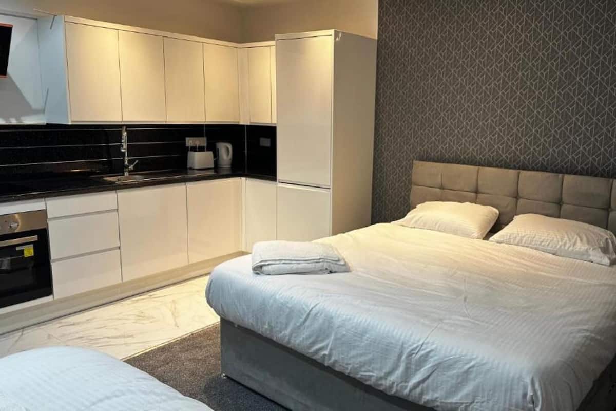 Ein modernes Hotelzimmer mit einem großen Bett, einer separaten Sitzecke, einer Küchenzeile und einer Wand mit Muster.