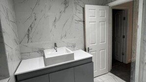 Une salle de bain moderne avec un pare-baignoire en marbre, un meuble-lavabo à deux vasques et une douche à paroi de verre.