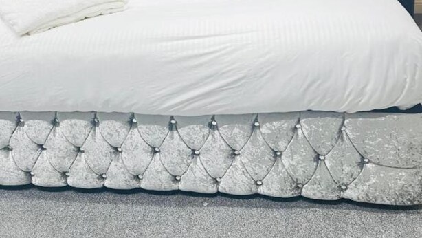 Un lit bien fait, doté d’une tête de lit capitonnée, de draps blancs et d’une bordure décorative au pied du lit.