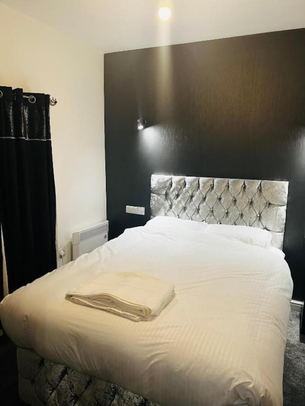 A hotel room with a large bed, a dark headboard, and a white comforter.
