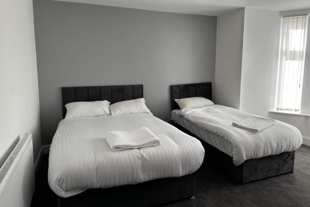 A bedroom with two beds, a radiator, and a window with curtains.