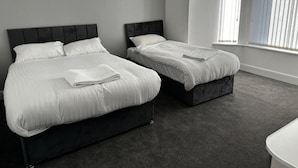 A bedroom with two beds, a dark headboard, and a window with blinds. - Cheetham Hill Guest House (Manchester)