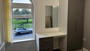 A room with a window, a mirror, a white desk, and a grey wardrobe. - Cheetham Hill Guest House (Manchester)