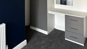 A bedroom with a dark blue wall, a grey wardrobe, a white dresser, and a ceiling light. - Cheetham Hill Guest House (Manchester)