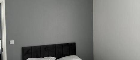 Une chambre à coucher avec un lit, des murs gris et une tête de lit sombre.