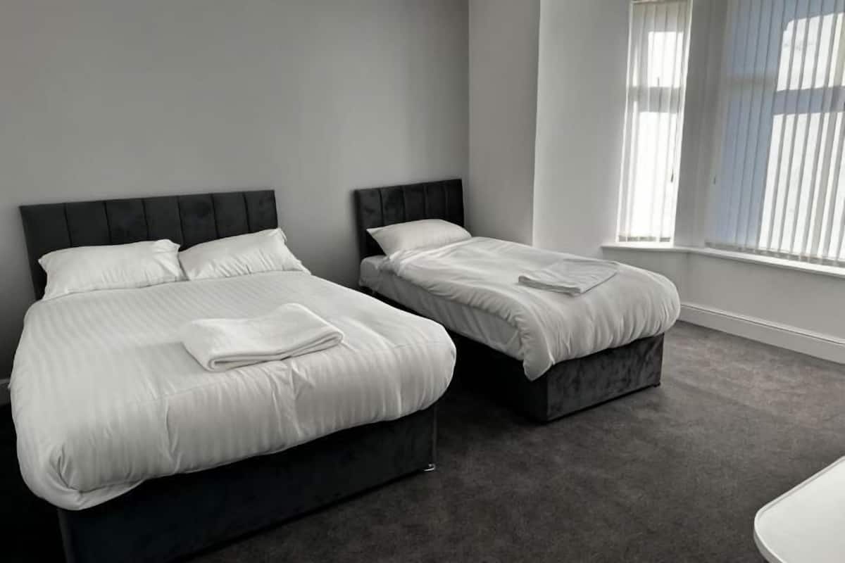 A hotel room with two beds, a large window with blinds, and a carpeted floor.