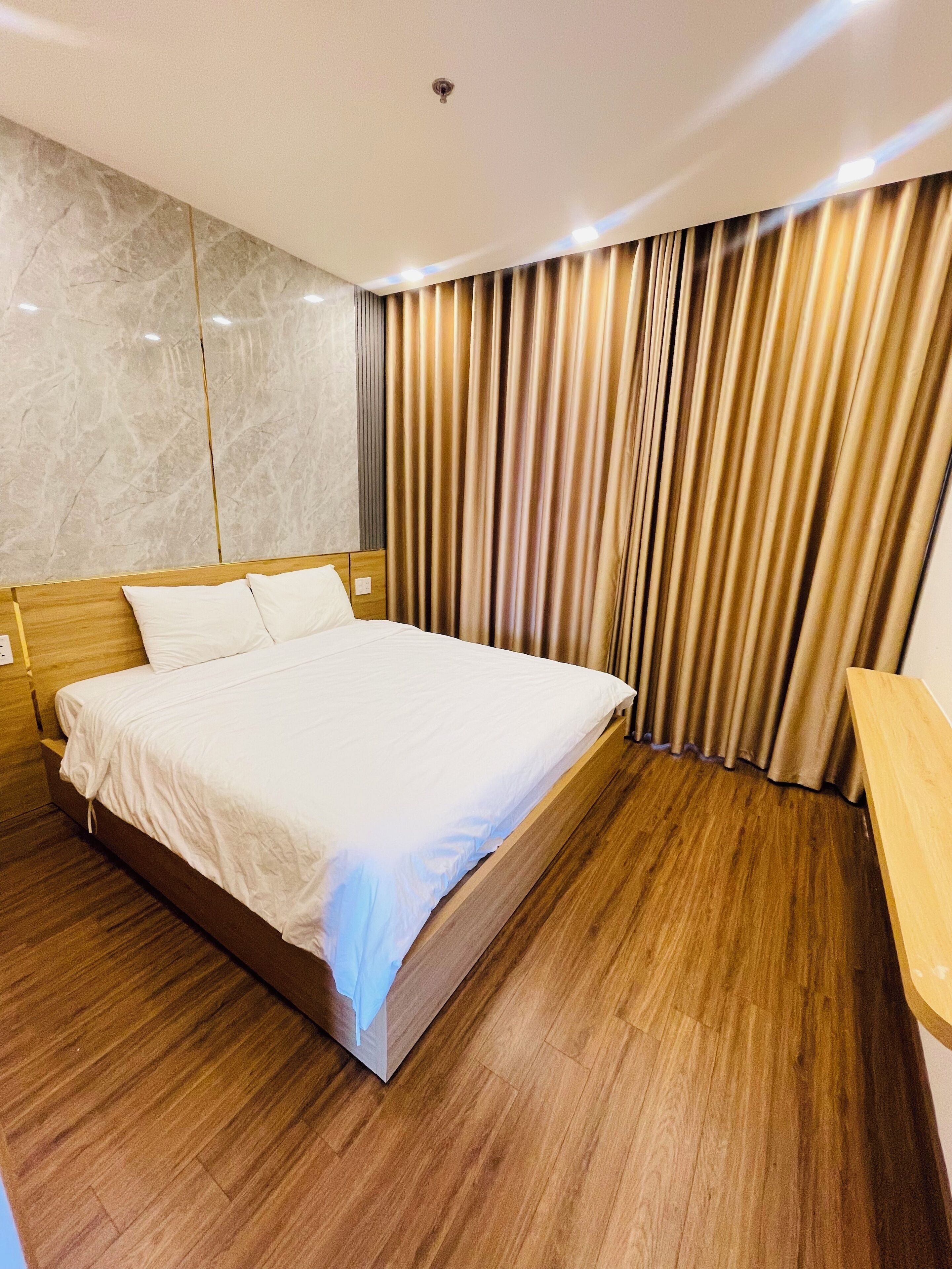 A modern hotel room with a wooden bed, a marble wall, and a curtain with vertical stripes.