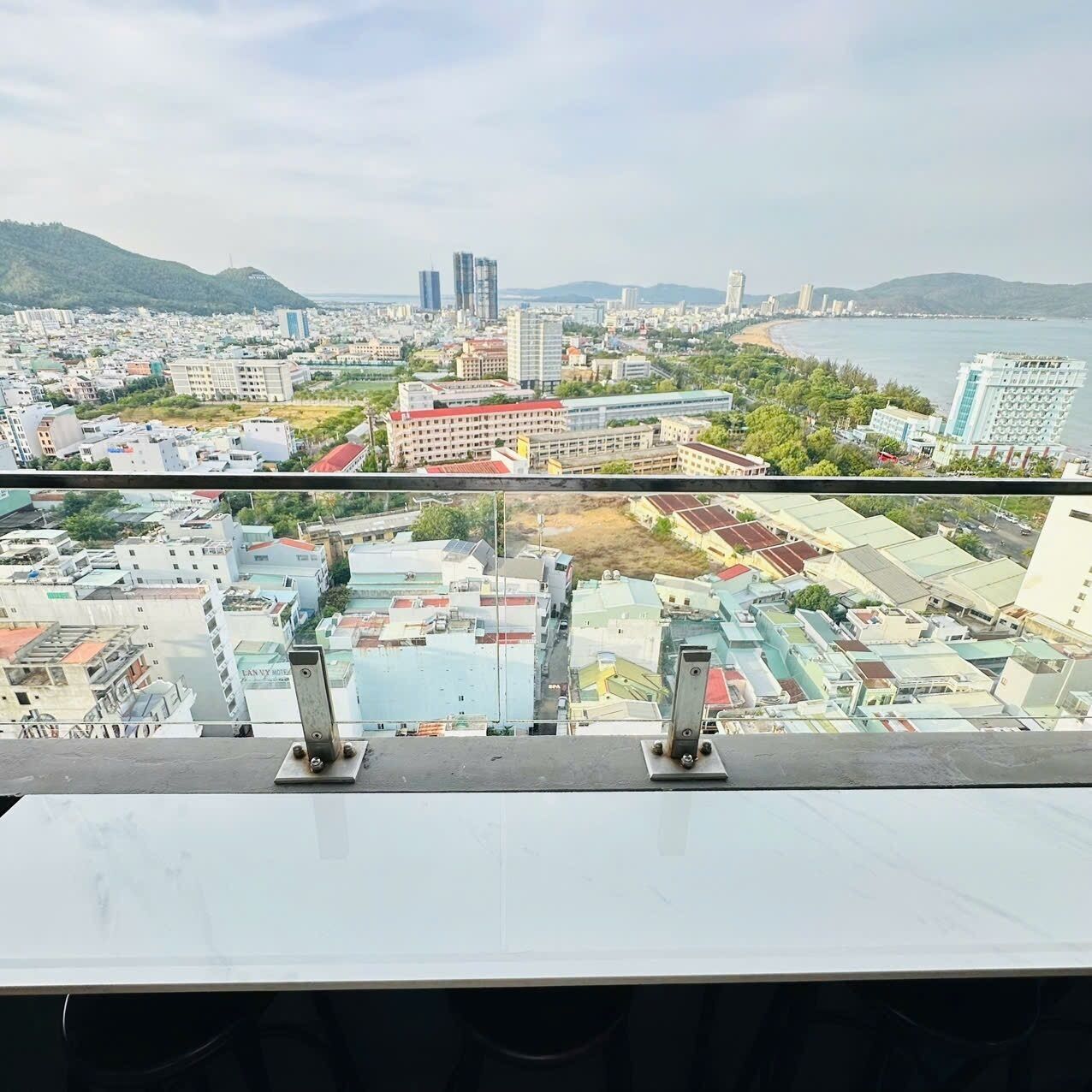 A panoramic view of a coastal city with modern buildings, a beach, and hills in the background.