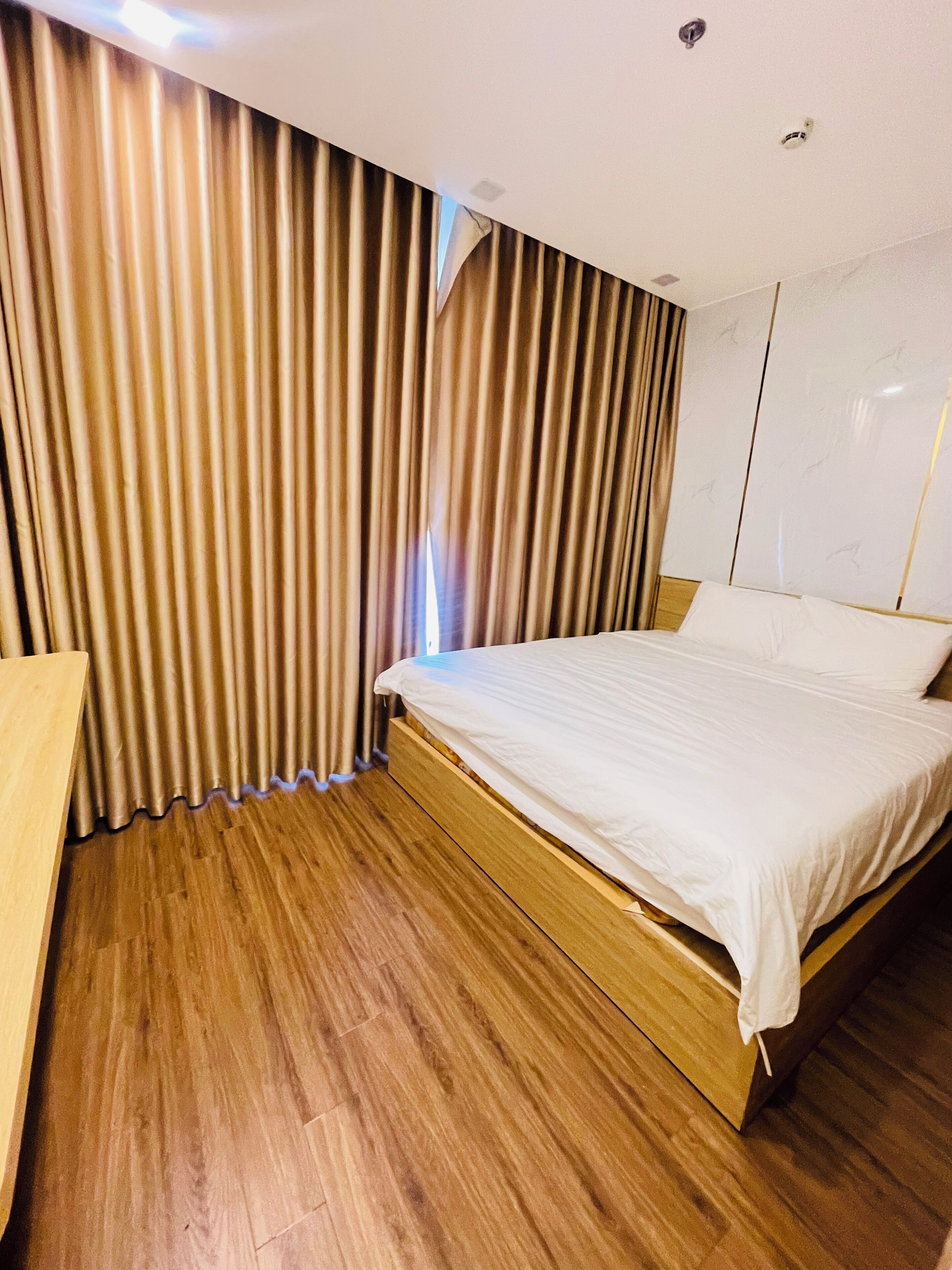 Een hotelkamer met een houten bed, een houten bureau en een groot raam met gordijnen.