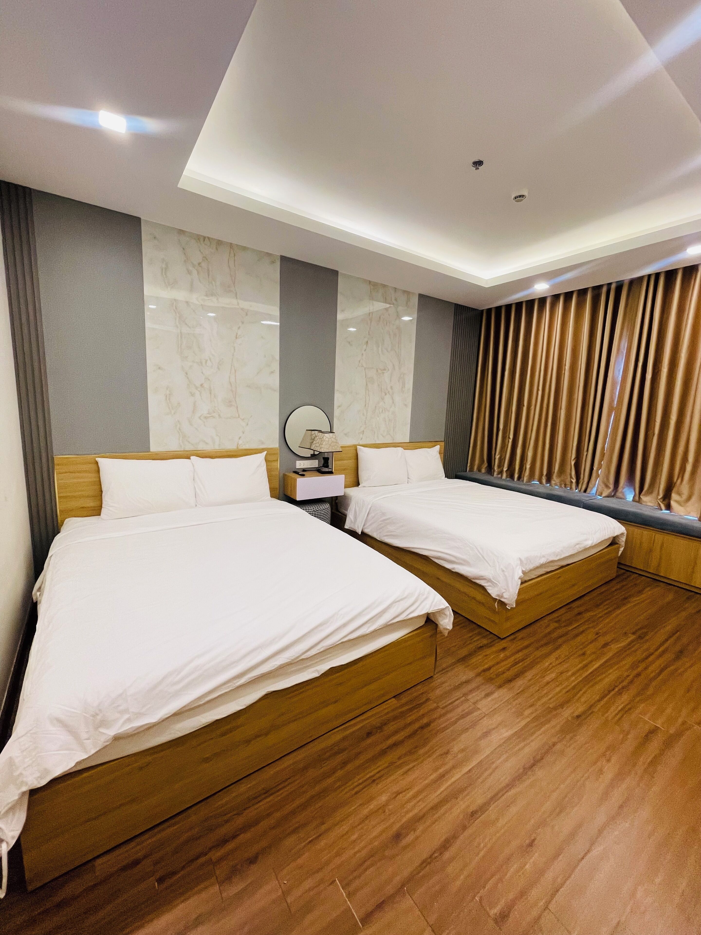 A hotel room with two beds, a marble wall, a wooden floor, and a window with curtains.
