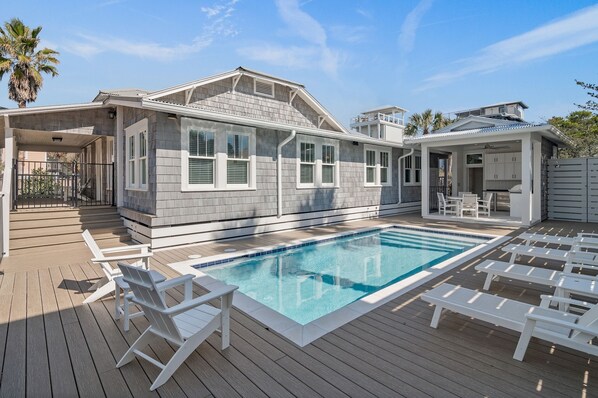 A modern house with a swimming pool, deck chairs, and a covered patio area.