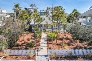 A pathway leading to a house with a porch, surrounded by various trees and shrubs.