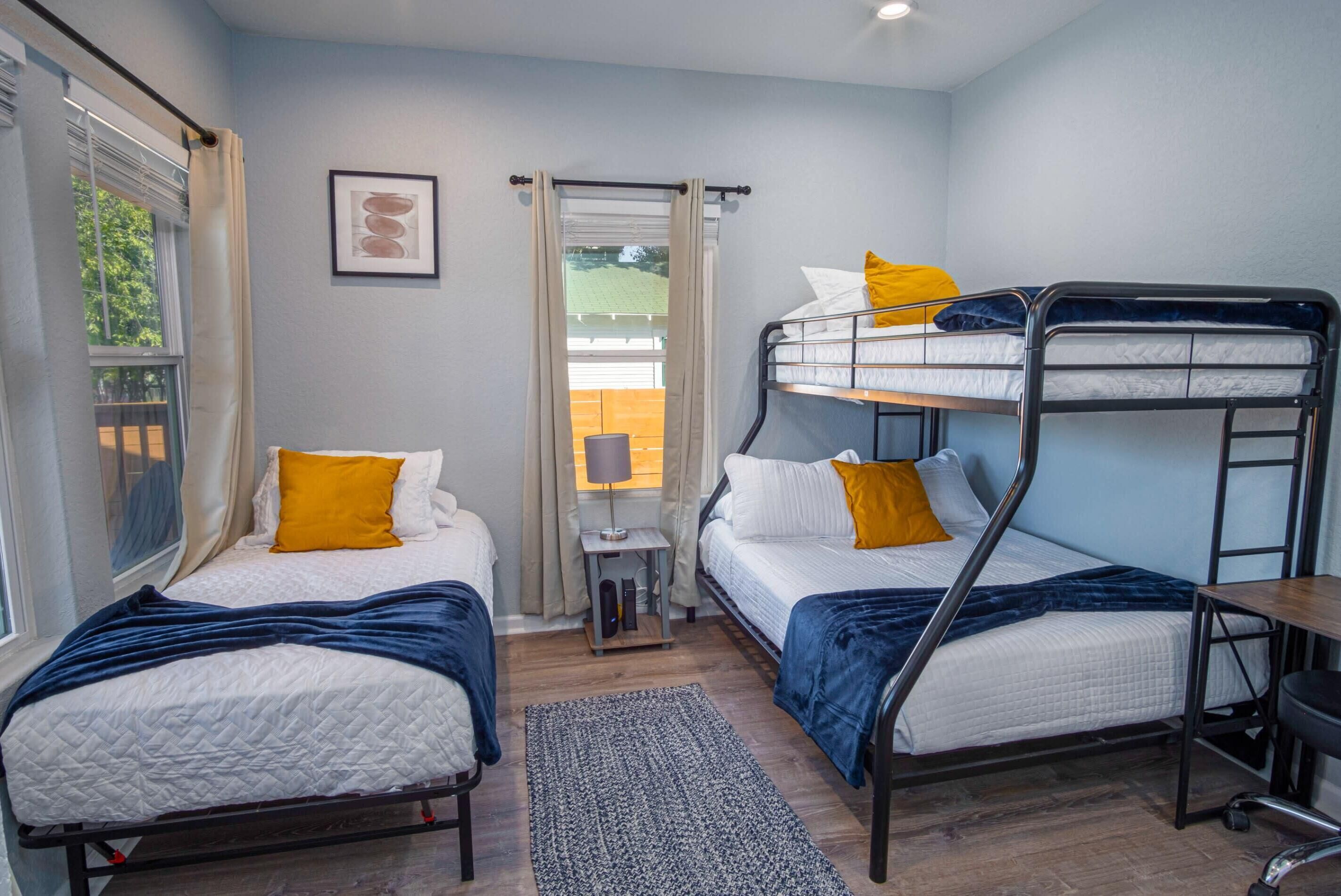 A compact room with two single beds and a bunk bed, a small table, a lamp, and a window with curtains.