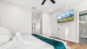Una habitación de hotel moderna con una cama grande, un plaid color turquesa y un televisor con imágenes de la ciudad en la pared.