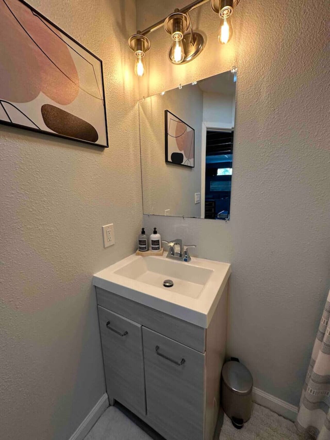 Un baño con un lavabo blanco, un espejo y una lámpara sobre el espejo.
