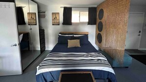 Un dormitorio con cama, armario, espejo y ventana.