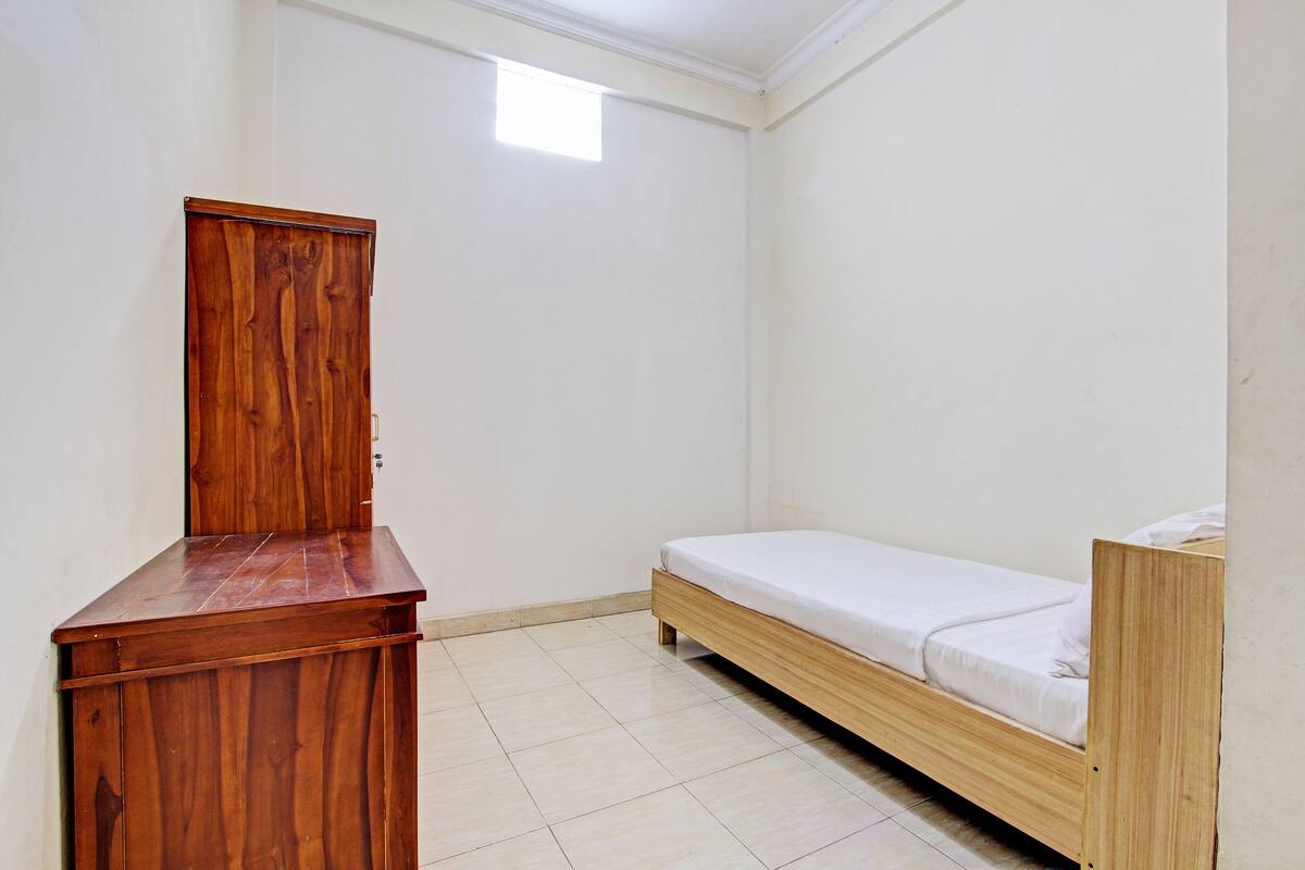 A small, single-room with a wooden desk, a bed, and a wardrobe.