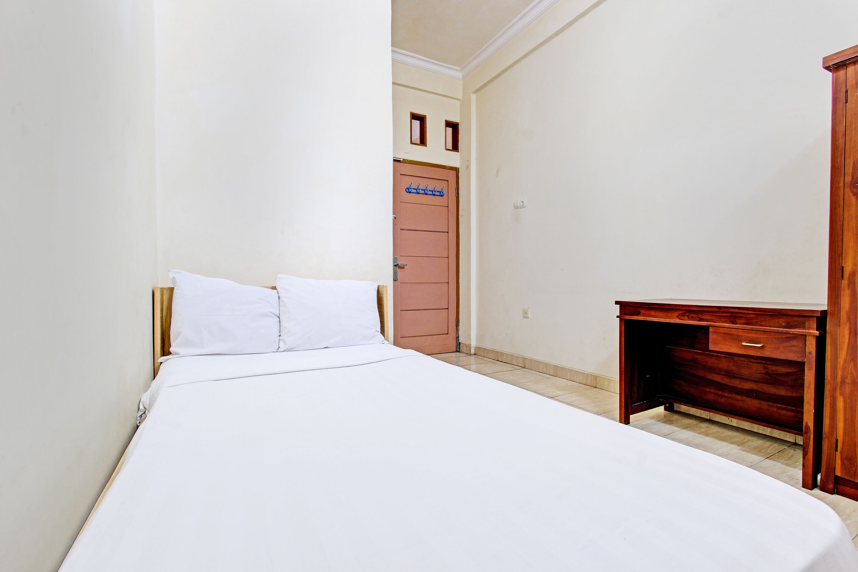 A bedroom with a bed, a wooden desk, and a door with a coat rack.