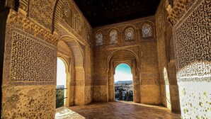 An interior with ornate arches and detailed carvings, a stone floor, and a view through an archway.