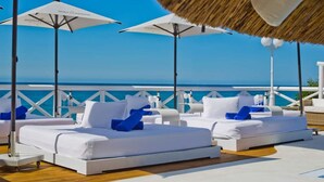 A deck with white lounge chairs and umbrellas, overlooking a clear blue sea.