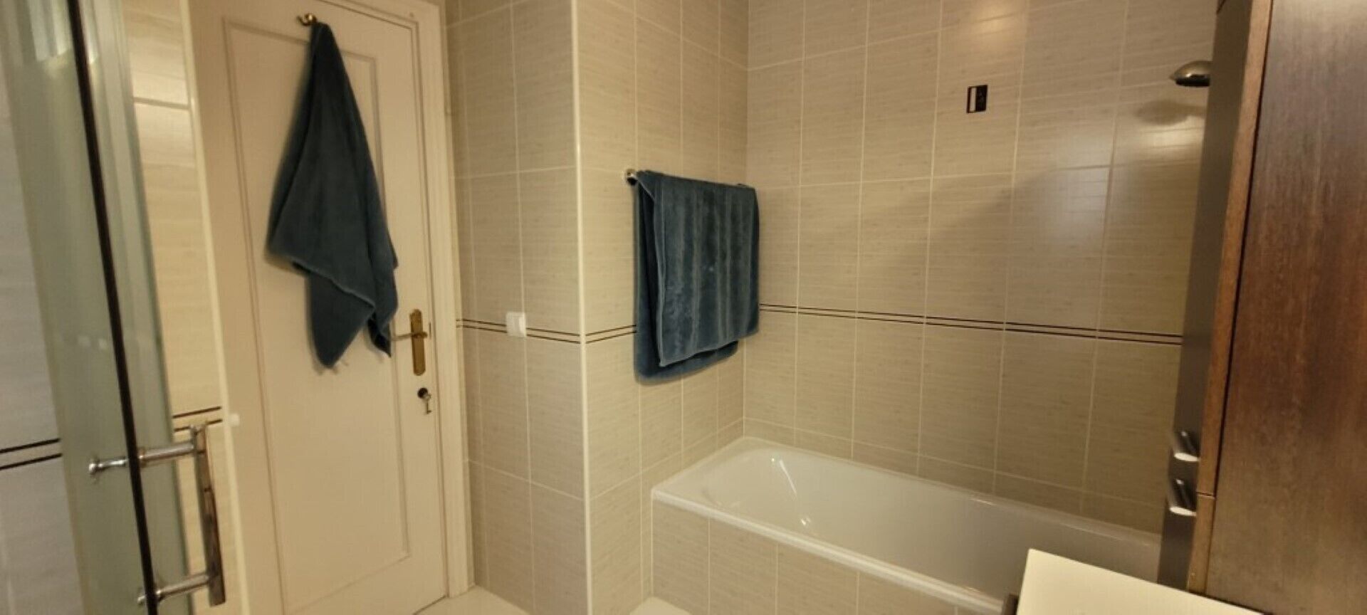 A bathroom with a bathtub, a glass shower enclosure, and a door with a towel hanging on it.
