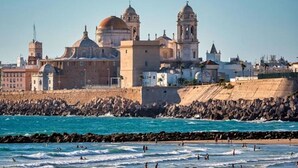 A coastal cityscape with a prominent historical building featuring domed architecture and a bell tower.