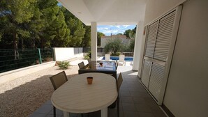 An outdoor patio with a round table and chairs, a small table with a cup, a pool, and a view of trees and buildings in the background. - SAONA VILLAS (VN OLIVE): villa for 10 people, private swimming pool, air co (Les Tres Cales)