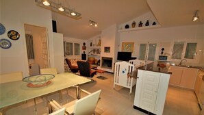 A modern kitchen with white cabinets, a dining area with a glass table, and a living space with a fireplace. - SAONA VILLAS (VN OLIVE): villa for 10 people, private swimming pool, air co (Les Tres Cales)