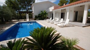 A swimming pool with lounge chairs, a covered patio, and a white building with a tiled roof. - SAONA VILLAS (VN OLIVE): villa for 10 people, private swimming pool, air co (Les Tres Cales)