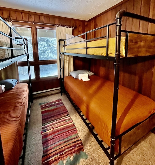 A bunk bed room with a window, a striped rug, and wooden walls. - SnowMonte in the Pines
(Dunmore)