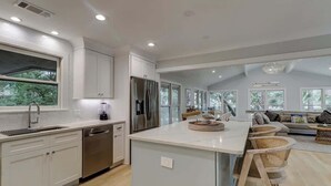 A modern kitchen with a central island, stainless steel appliances, and a dining area with wicker chairs.