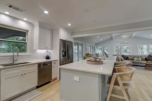 Una cocina moderna con una isla central, electrodomésticos de acero inoxidable y un comedor con sillas de mimbre.